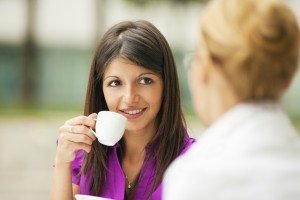 A woman speaking to another woman over a cup of coffee